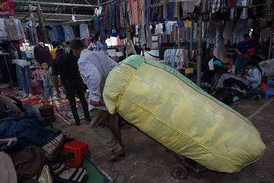 古着を業者が重そうに倉庫へ運ぶ（カンボジア・シェムリアップのルー市場で）