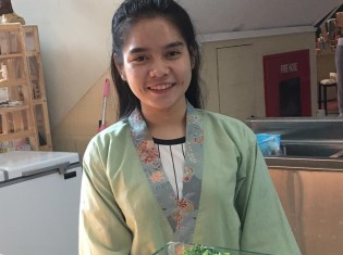 ラッキーモールの総菜屋で働くクロワットさん（21歳、女性）。来世では美しく、良い香りのする女性になりたいという願いを込めて、いつも仏様には蓮の花を手向けているという