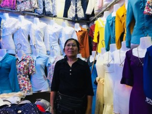 カンボジア・シェムリアップにある「プサー・ルー（ルー市場）」で既製服店を営むキム・ヘアンさん。下着から伝統衣装までさまざまな服が並ぶ店内は華やかだ