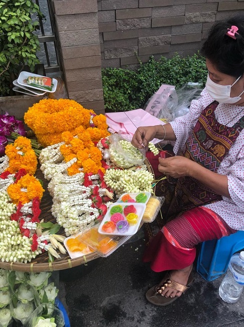 BTSオンヌット駅付近の路上でお供え用の花を売る女性。深夜２時から買い出しへ行き、販売時間中も花輪を作り続ける。遅いときには夜11時まで売り続ける