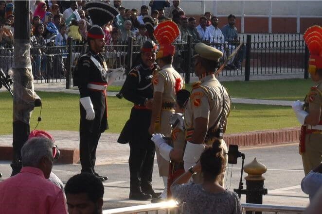 国旗降納後、国境越しに笑顔で握手を交わす印パの国境警備隊。オリーブ色の服がインド、黒色の服がパキスタン。握手をする国境警備隊の足元に見える白線が国境線