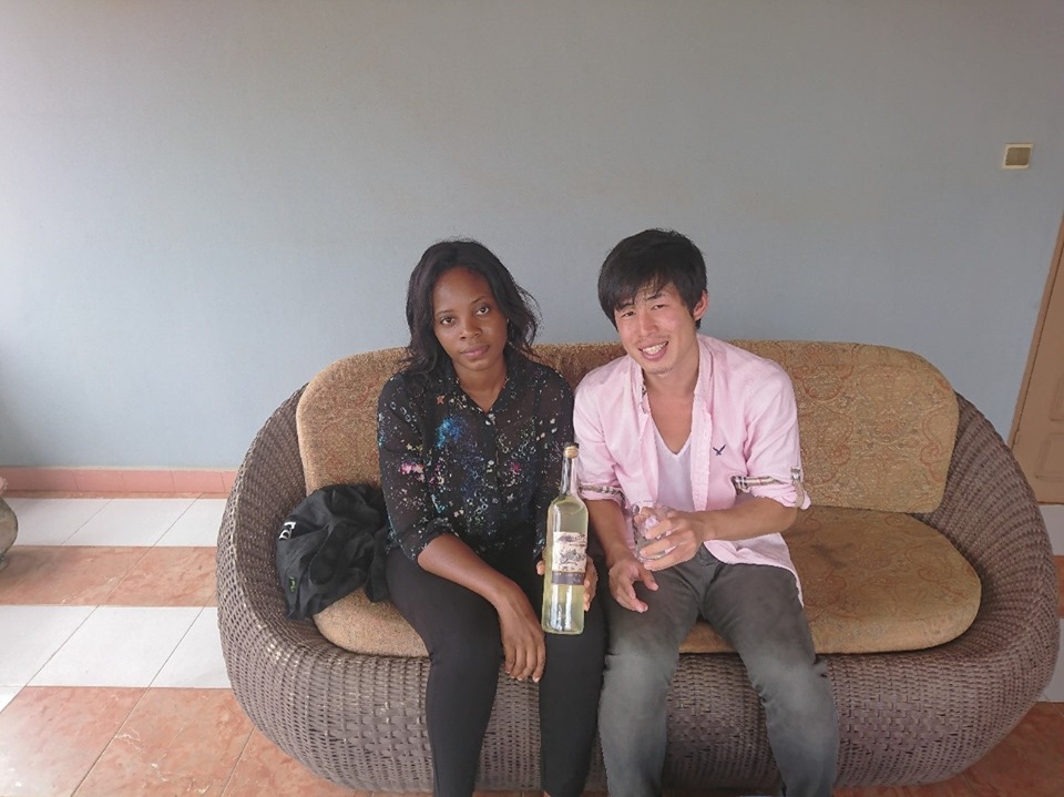 リロリアさん（左）と筆者（右）。トウモロコシ酒を試飲した筆者はベナンのお土産に2本購入した（ベナン・アボメカラビのホテルで撮影）