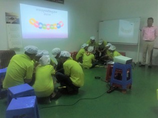 カンボジアの経済特区にある工場で、RIC（報・連・相）研修の一環として「輪っかゲーム」に真剣に取り組む参加者たち
