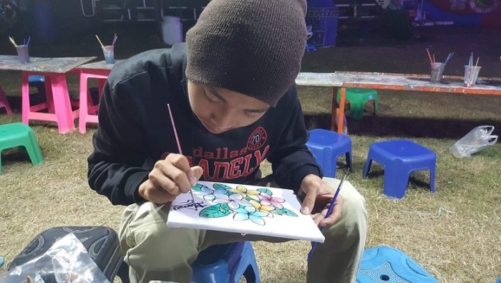 メーソットマーケットで草花の絵を描くブワイ。ブワイが植物に興味をもったきっかけは、タイ側の難民キャンプの中で日本のNGOシャンティ国際ボランティア会（SVA）が運営する図書館で読み漁っていた本だという