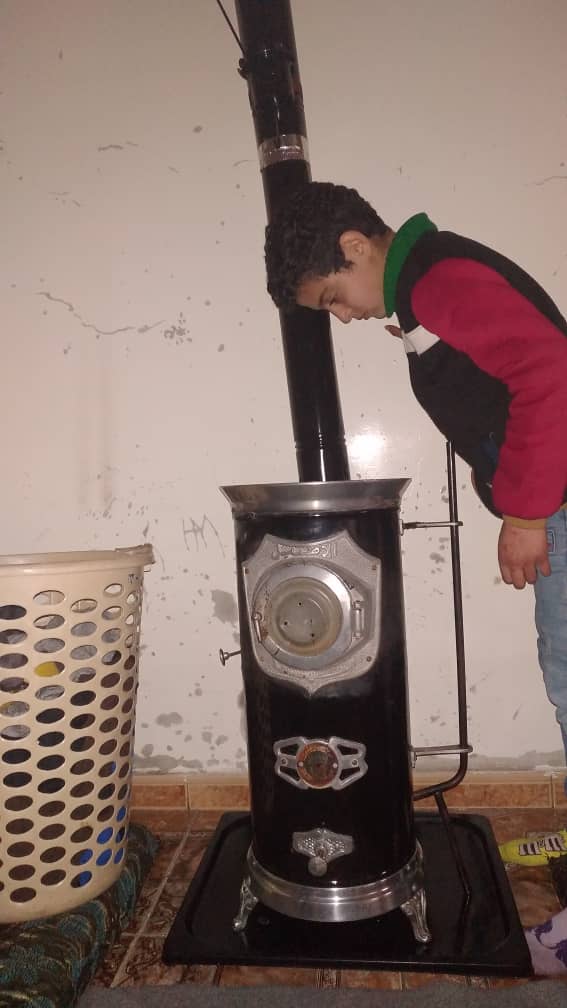 ストーブをのぞき込むサラーハくん。灯油を買うお金がなく、古着などをくべて暖をとる（シリア・アレッポ、2022年1月）
