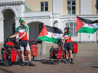サハラ・アラブ民主共和国のライダースーツに身を包むゴドビさん（右）とラドラさん（左）。自転車の後ろで国旗がはためく